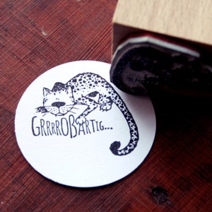 Könnte beinhalten: Eine Schwarzweißillustration einer gefleckten Katze mit dem Text "GRRRROBARTIG..." auf einem weißen runden Aufkleber.