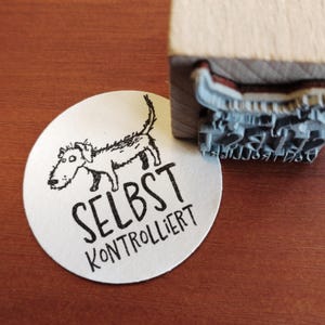 Könnte beinhalten: Ein weißer runder Aufkleber mit einer Schwarzweißillustration eines Hundes und dem Text "SELBST KONTROLLIERT".