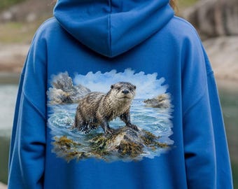 May include: A bright blue hooded sweatshirt featuring a detailed graphic print on the back. The print depicts a brown otter standing on a rock in the middle of a body of water, surrounded by splashes and rocky terrain in a natural outdoor setting.