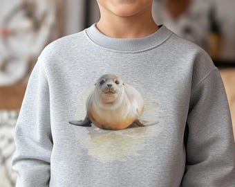 May include: A light gray crewneck sweatshirt featuring a centered graphic of a brown seal pup resting on a sandy beach. The long-sleeved pullover has a ribbed neckline, cuffs, and hem, providing a simple and clean look for casual daily wear.