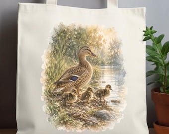 May include: A cream-colored canvas tote bag featuring a printed illustration of a mother duck with three ducklings standing by a riverbank. The artwork displays soft, natural tones of brown, green, and blue, depicting a serene outdoor scene.