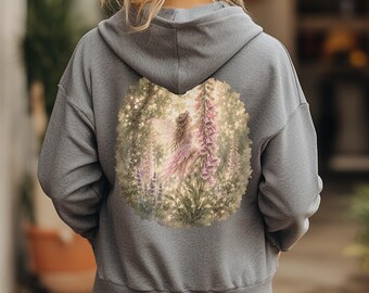 May include: A heather gray hooded sweatshirt featuring a large circular graphic on the back. The print depicts a fairy with wings standing among tall pink foxglove flowers and lush green foliage in a soft, painterly, and muted color palette.