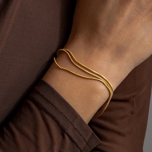 May include: A gold chain bracelet with two strands. The bracelet is worn on a person's wrist.