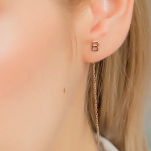 May include: A gold initial 'B' earring with a delicate chain dangling from the bottom.