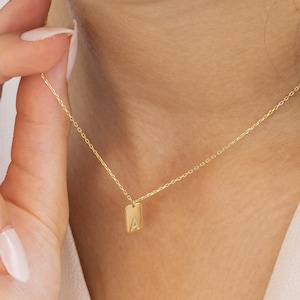 Op de afbeelding: Een gouden ketting met een klein rechthoekig hangertje met de letter 'A'.
