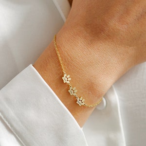 May include: Gold chain bracelet with four paw print charms. Each charm has a different name engraved on it.