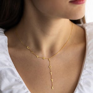 May include: A gold-colored necklace spelling out the name "CHARLOTTE" in individual capital letters. The necklace has a delicate chain and the letters are aligned in a stylish, personalized design.