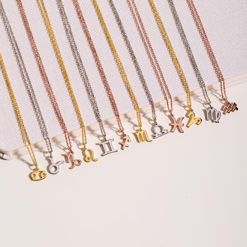 May include: A set of 12 gold, silver, and rose gold necklaces with zodiac signs as pendants. The signs are: Cancer, Leo, Virgo, Libra, Scorpio, Sagittarius, Capricorn, Aquarius, Pisces, Aries, Taurus, and Gemini.