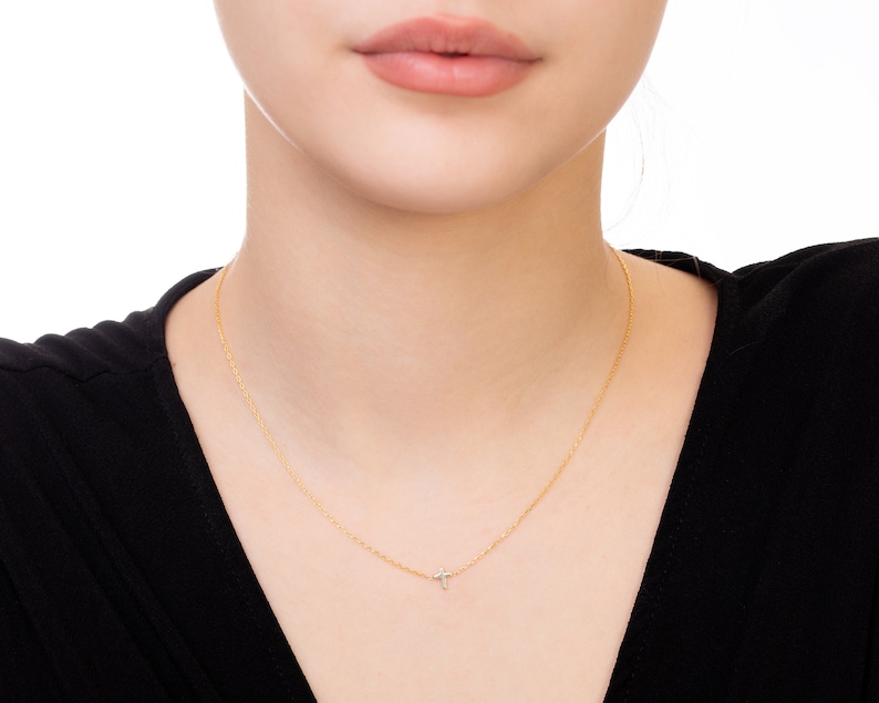 Pu&ograve; includere: Una delicata collana d'oro con un piccolo pendente a forma di croce. La collana &egrave; indossata su un top nero, creando un contrasto che mette in risalto il gioiello. Il pendente a forma di croce sembra avere piccoli dettagli scintillanti.