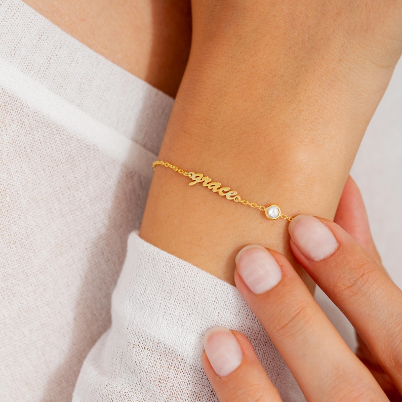 May include: Gold chain bracelet with the word "grace" in cursive script and a small clear crystal charm.
