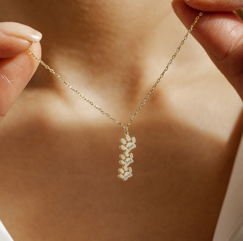 Op de afbeelding: Gouden ketting met een bedel van gestapelde hondenpootafdrukken, elk gegraveerd met de naam van een hond: Max, Rex en Ruby.