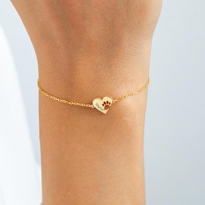 May include: Gold-coloured bracelet with a heart-shaped charm. The charm has a paw print and the name "Marley" engraved. The bracelet is delicate and made of a fine chain.