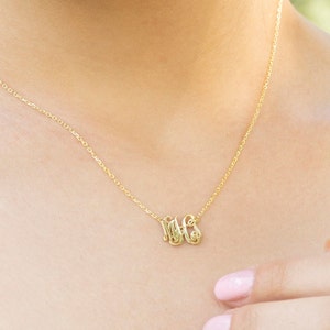 May include: A gold chain necklace with a delicate pendant featuring the letters "MGS" in a cursive script.