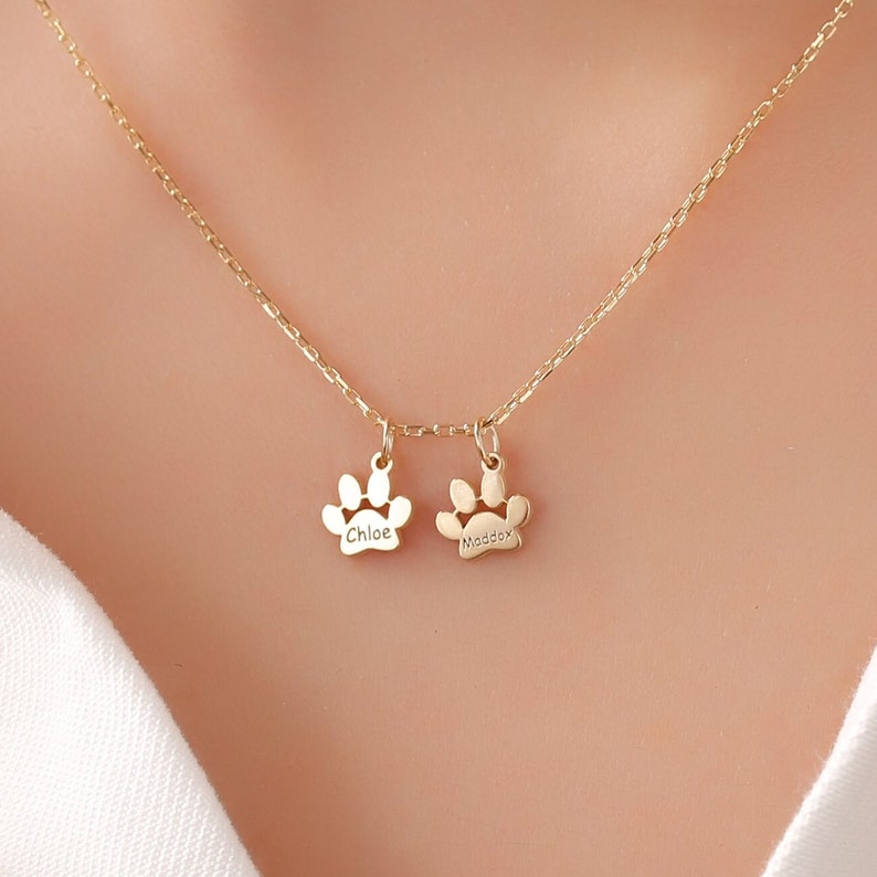 May include: Gold necklace with two paw print charms, one engraved with "Chloe" and the other with "Maddox".