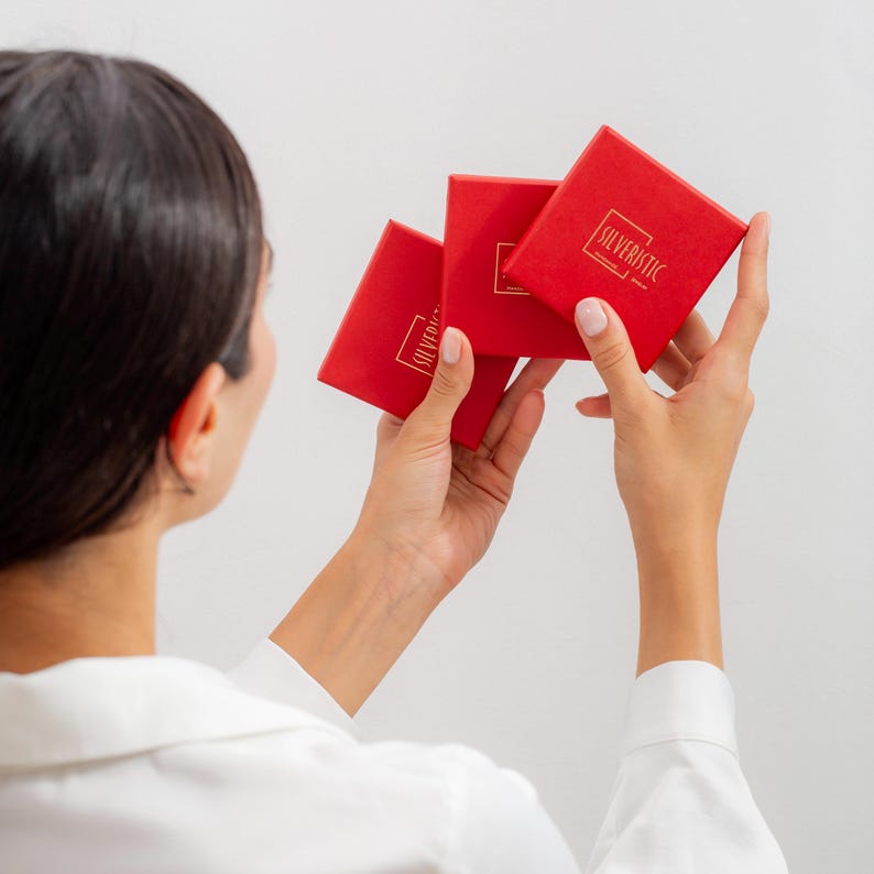 May include: Three red boxes with the text "SILVERISTIC" in gold lettering. The boxes are being held by a person.