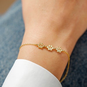 May include: Gold paw print charm bracelet with the names "Juno", "Kiko", and "Barney" engraved on each charm.