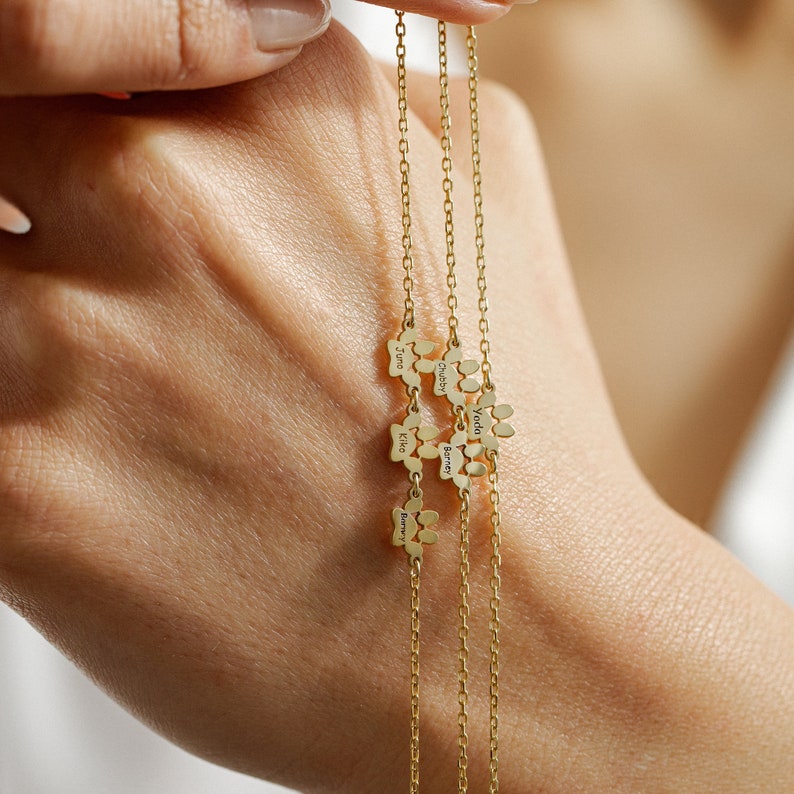 May include: Three gold chains with paw print charms, each charm engraved with a different name: Juno, Chester, Yoda, Barnes, Kiko, and Barry.