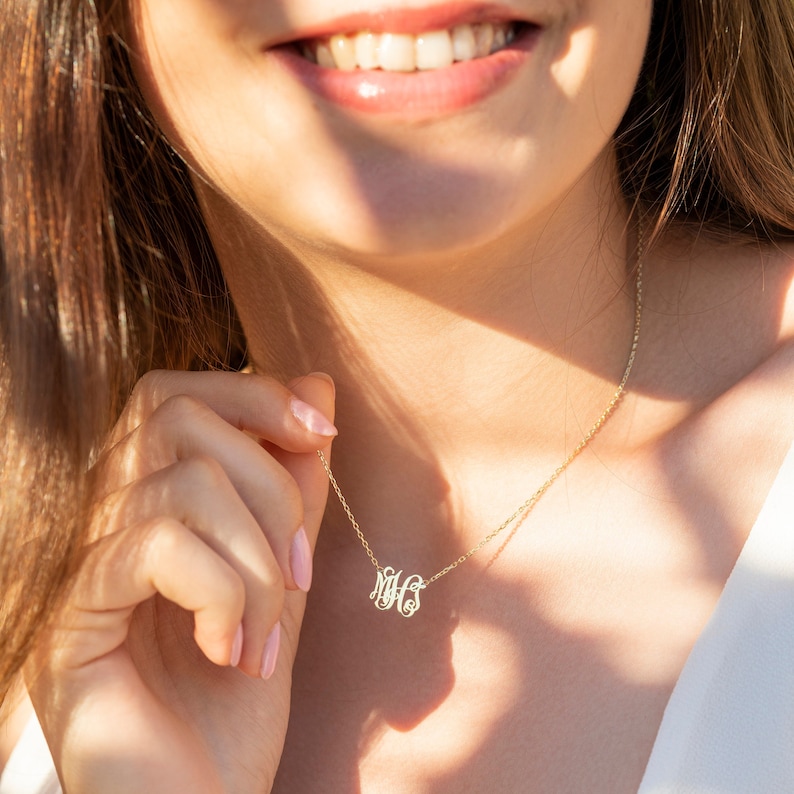 May include: A gold necklace with a delicate monogram pendant. The pendant features the letters "MHS" in a script font.