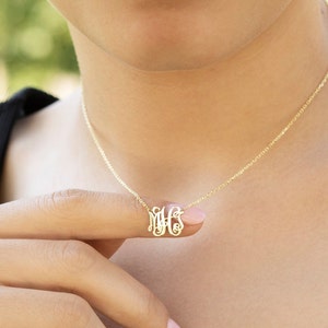 May include: A gold chain necklace with a delicate monogram pendant. The pendant features the letters M, H, and S intertwined.