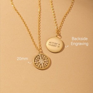 May include: Gold-coloured necklaces. One pendant features a compass design, 20mm in diameter, the other has engraved coordinates. The backside engraving is visible on one pendant. The compass pendant has a detailed design.