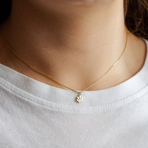 Op de afbeelding: Een gouden ketting met een klein hangertje in de vorm van een poot. De ketting wordt gedragen door iemand met een wit shirt.