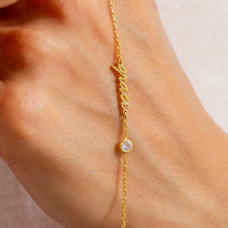 May include: A gold chain bracelet with the word "grace" in cursive and a small clear rhinestone charm.