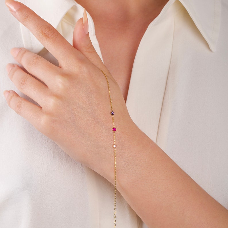 May include: A gold chain bracelet with three small gemstones: a pink, a purple, and a white.