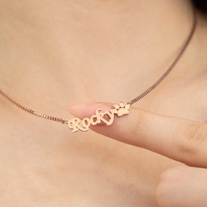 May include: A rose gold necklace with a personalized nameplate that reads "Rocky" and a paw print charm.