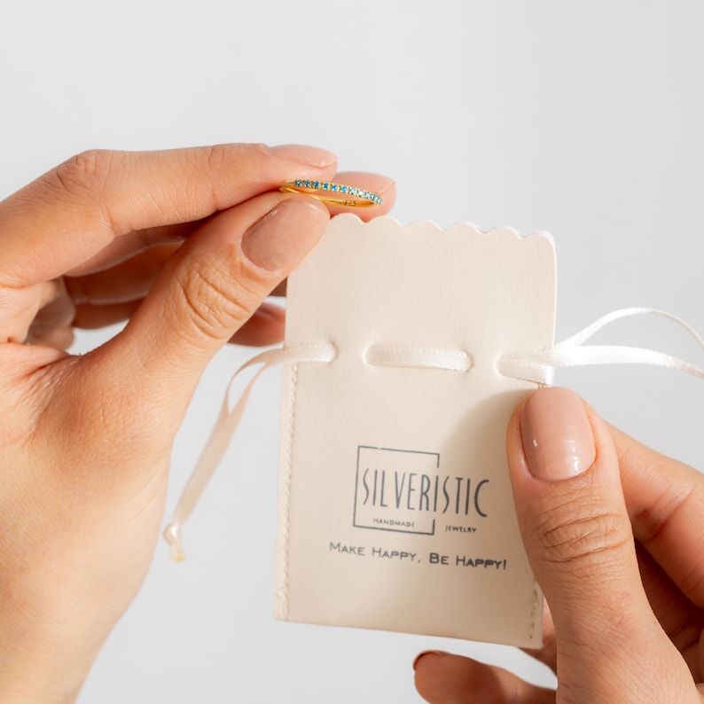 May include: A delicate gold ring with a thin band of turquoise gemstones. The ring is displayed in a white velvet pouch with the text "Silveristic Handmade Jewelry Make Happy, Be Happy!"