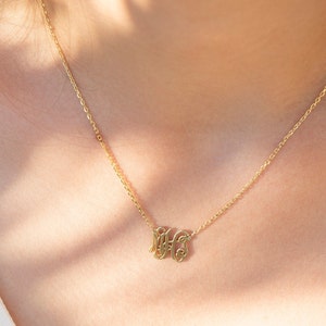 May include: A gold chain necklace with a delicate pendant featuring the initials "MHS" in a cursive script.