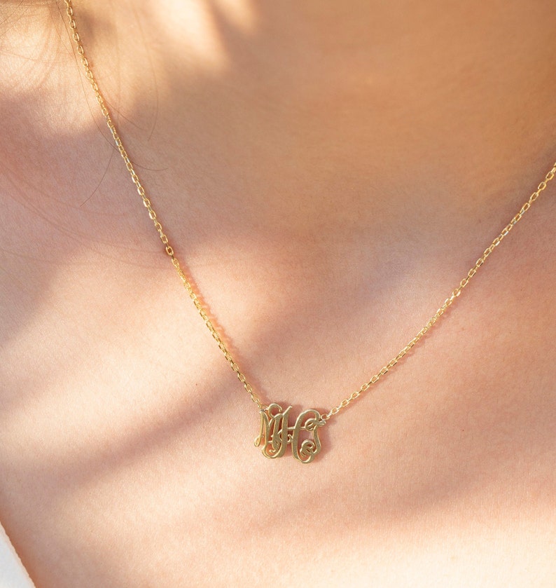 May include: A gold chain necklace with a delicate pendant featuring the initials "MHS" in a cursive script.