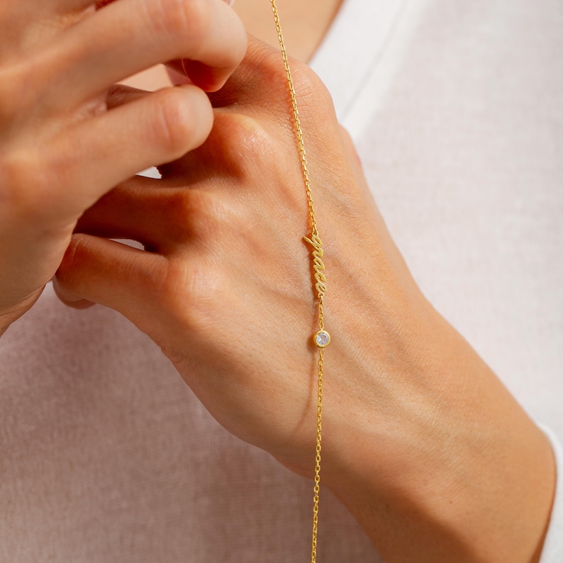 May include: A gold chain necklace with the word "peace" written in cursive and a small clear crystal charm.