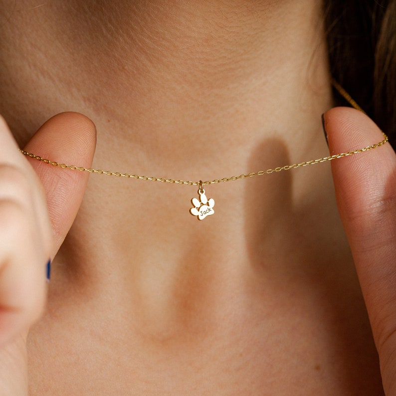 Op de afbeelding: Een gouden ketting met een kleine gouden pootprint bedel. De bedel heeft de naam "Jack" gegraveerd.
