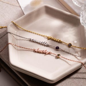 May include: Three delicate gold, silver, and rose gold necklaces with small gemstones. Each necklace features a name, "grace", "camille", and "katelyn", written in cursive.