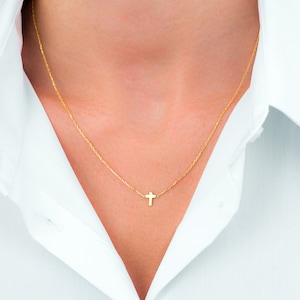 Pu&ograve; includere: Una delicata collana color oro con un piccolo pendente a forma di croce. La collana &egrave; indossata su una camicia bianca con colletto. La croce &egrave; appesa a una sottile catena, creando un look semplice ed elegante.