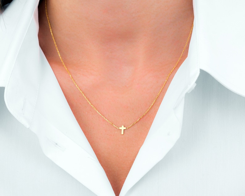 Pu&ograve; includere: Una delicata collana color oro con un piccolo pendente a forma di croce. La collana &egrave; indossata su una camicia bianca con colletto. La croce &egrave; appesa a una sottile catena, creando un look semplice ed elegante.