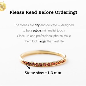 May include: A delicate gold ring with a row of tiny red gemstones. The ring is shown on a white background. Stone size: ~1.3 mm.