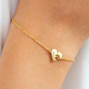 May include: A delicate gold bracelet with a heart-shaped charm. The charm has a paw print cutout and the name "Marley" engraved. The bracelet is attached to a fine chain.