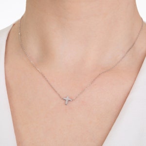 Pu&ograve; includere: Una delicata collana d'argento con un piccolo pendente a forma di croce. La croce &egrave; posizionata leggermente decentrata su una catena sottile. La collana &egrave; esposta su sfondo bianco.