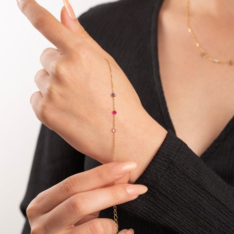 May include: A gold chain bracelet with three small gemstones: a pink, a red, and a purple.