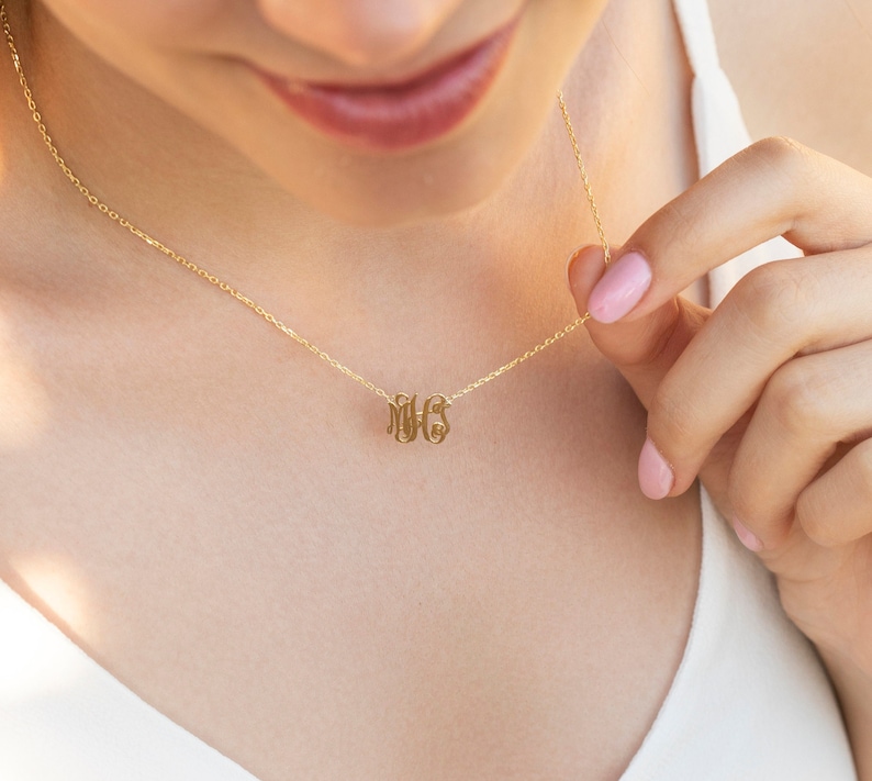 May include: A gold chain necklace with a delicate monogram pendant featuring the letters "MHS".