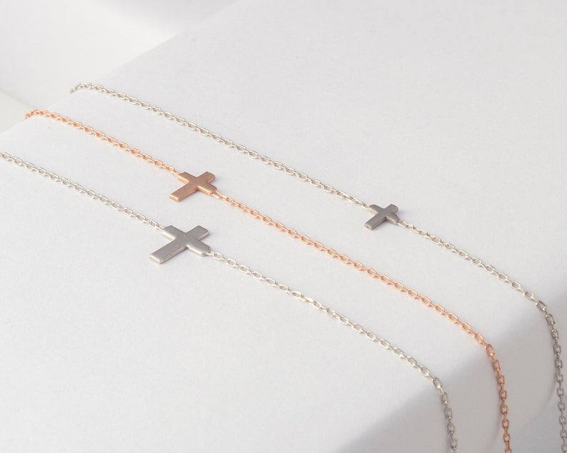 Pu&ograve; includere: Quattro delicate collane con croci in argento e oro rosa. Ogni collana presenta un piccolo ciondolo a forma di croce attaccato a una sottile catena. Le collane sono esposte su una superficie bianca, mettendo in risalto il loro design minimalista e l'elegante semplicit&agrave;.
