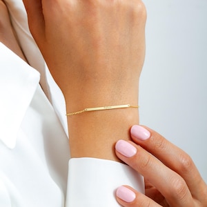 May include: A gold chain bracelet with a thin, flat bar charm engraved with the word "Sophia".