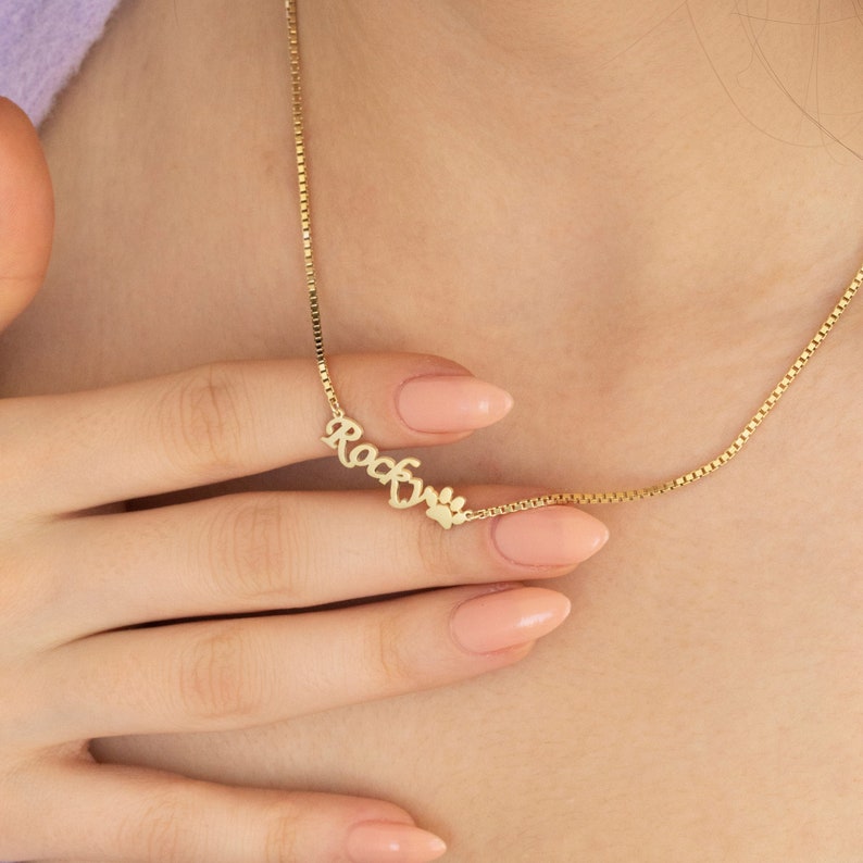 May include: Gold necklace with a nameplate that says "Rocky" and a paw print charm.