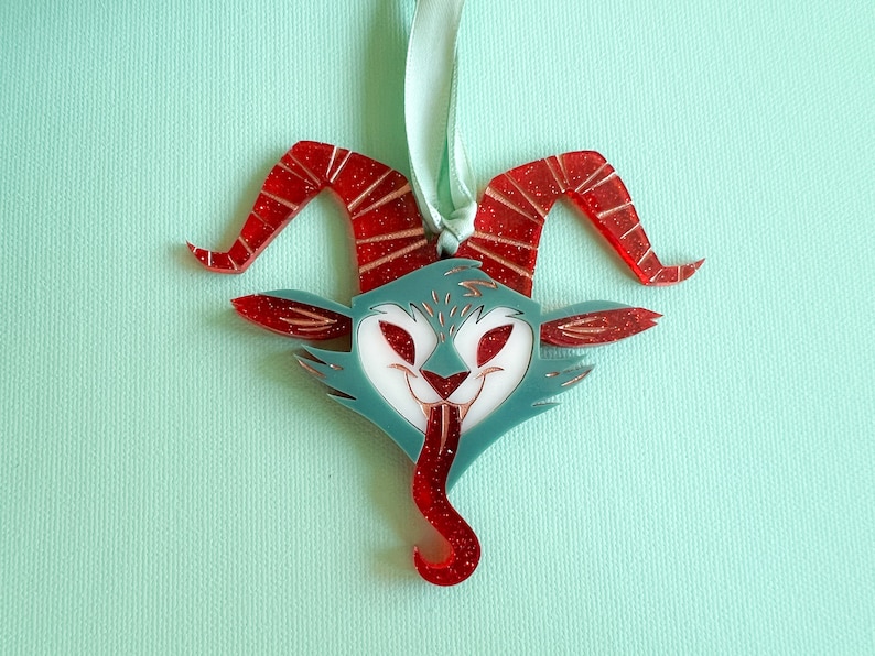 May include: Red and blue glitter ornament shaped like a horned creature with a wide, toothy grin and a long, curled tongue.