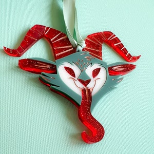 May include: Red and white glitter ornament shaped like a cartoonish demon with horns and a tongue sticking out.