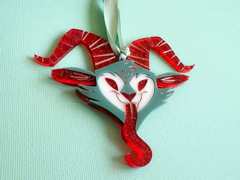 May include: Red and white glitter ornament shaped like a cartoonish demon with horns and a tongue sticking out.