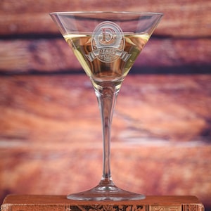 May include: A clear glass martini glass with a gold-colored drink. The glass is engraved with a monogram of the letter "D" and the name "DARY" in a decorative font.