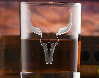 May include: A clear glass tumbler with an etched bull skull design. The glass is filled with amber-colored liquid.