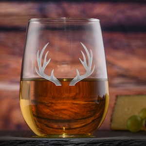 May include: A clear glass with an etched design of antlers. The glass is filled with a dark amber liquid.